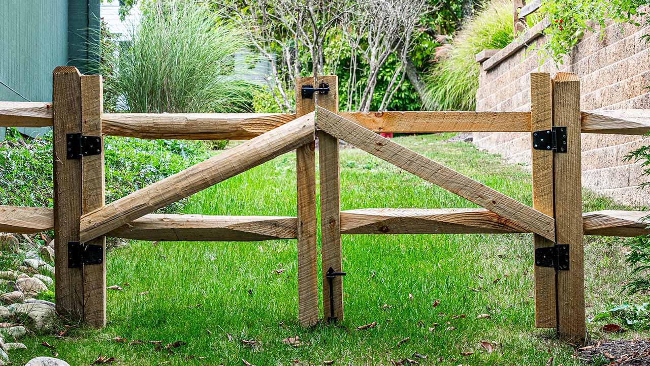 Split-rail gate with wide rail gaps beside a lawn and stone wall