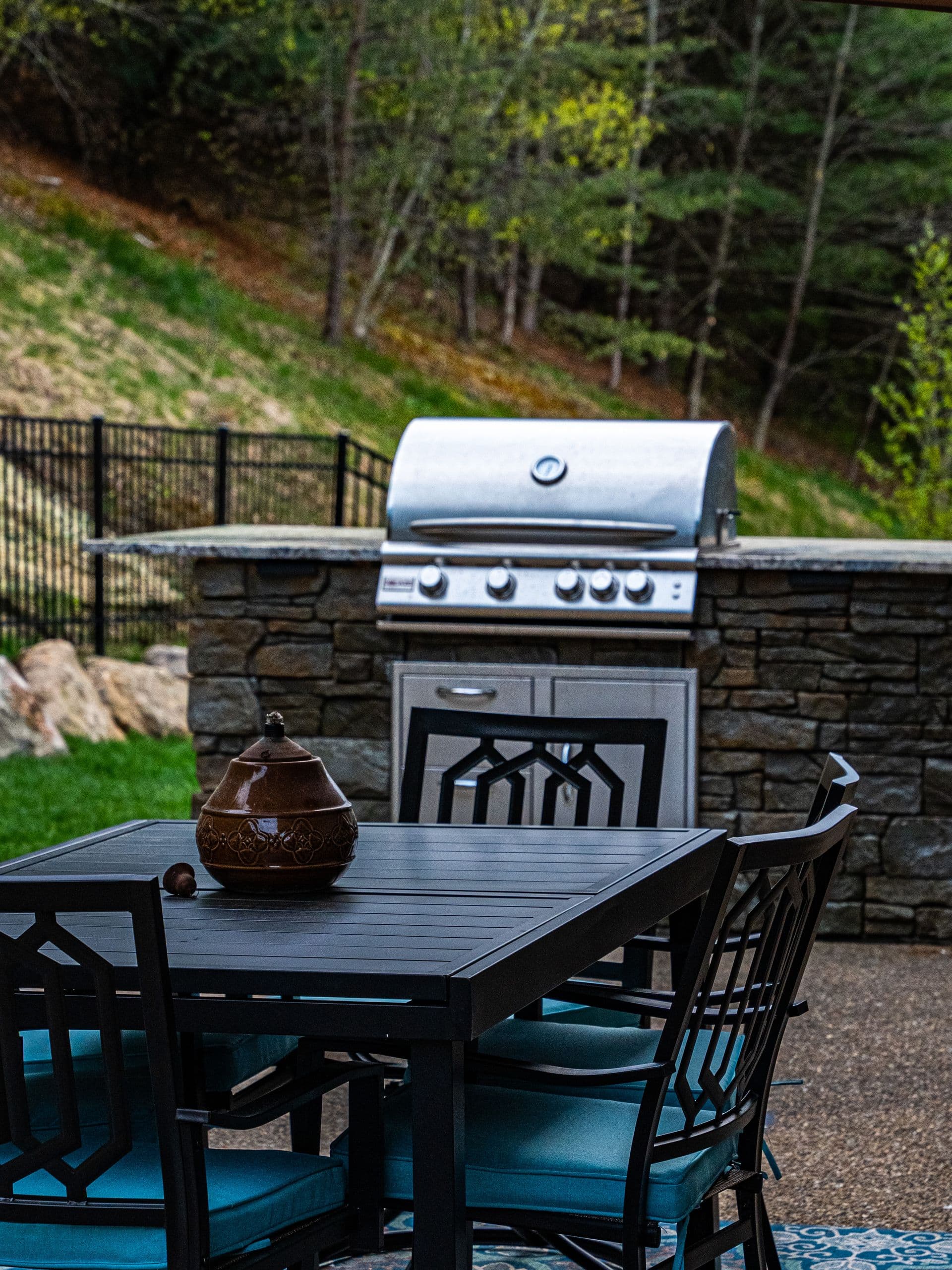 Stone outdoor kitchen with a built-in stainless grill and granite counter beside a covered dining set