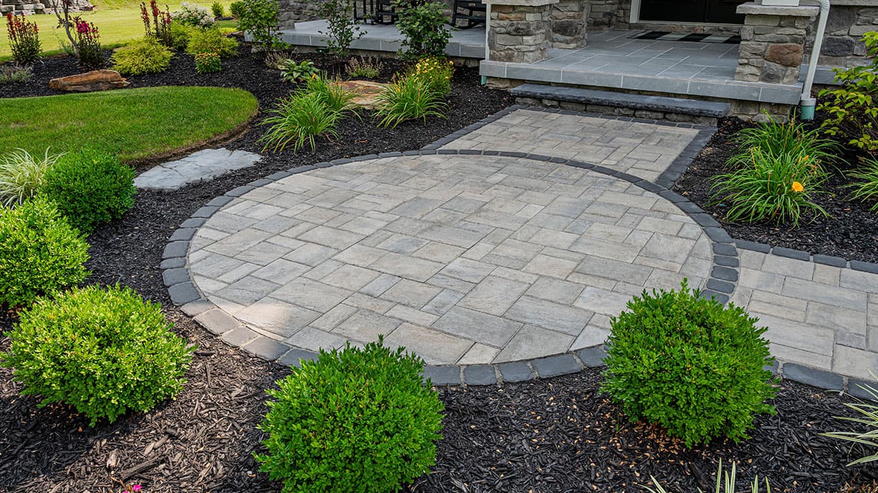 Circular paver patio with a dark soldier-course border, joined to the house by a paver walkway