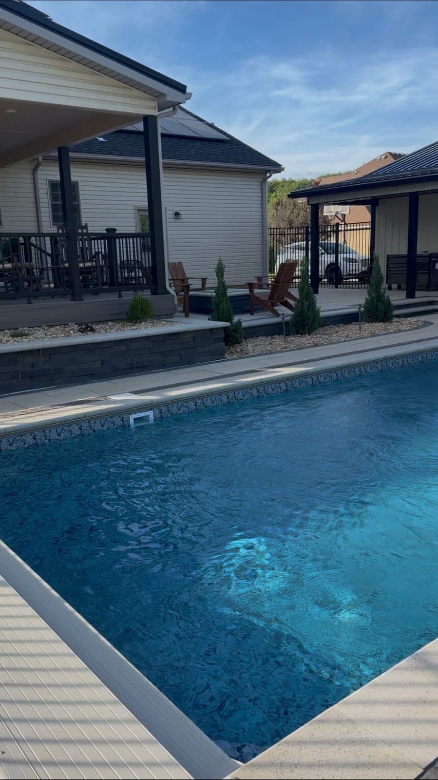 Pool alongside stacked-stone retaining wall and pergola-covered patio
