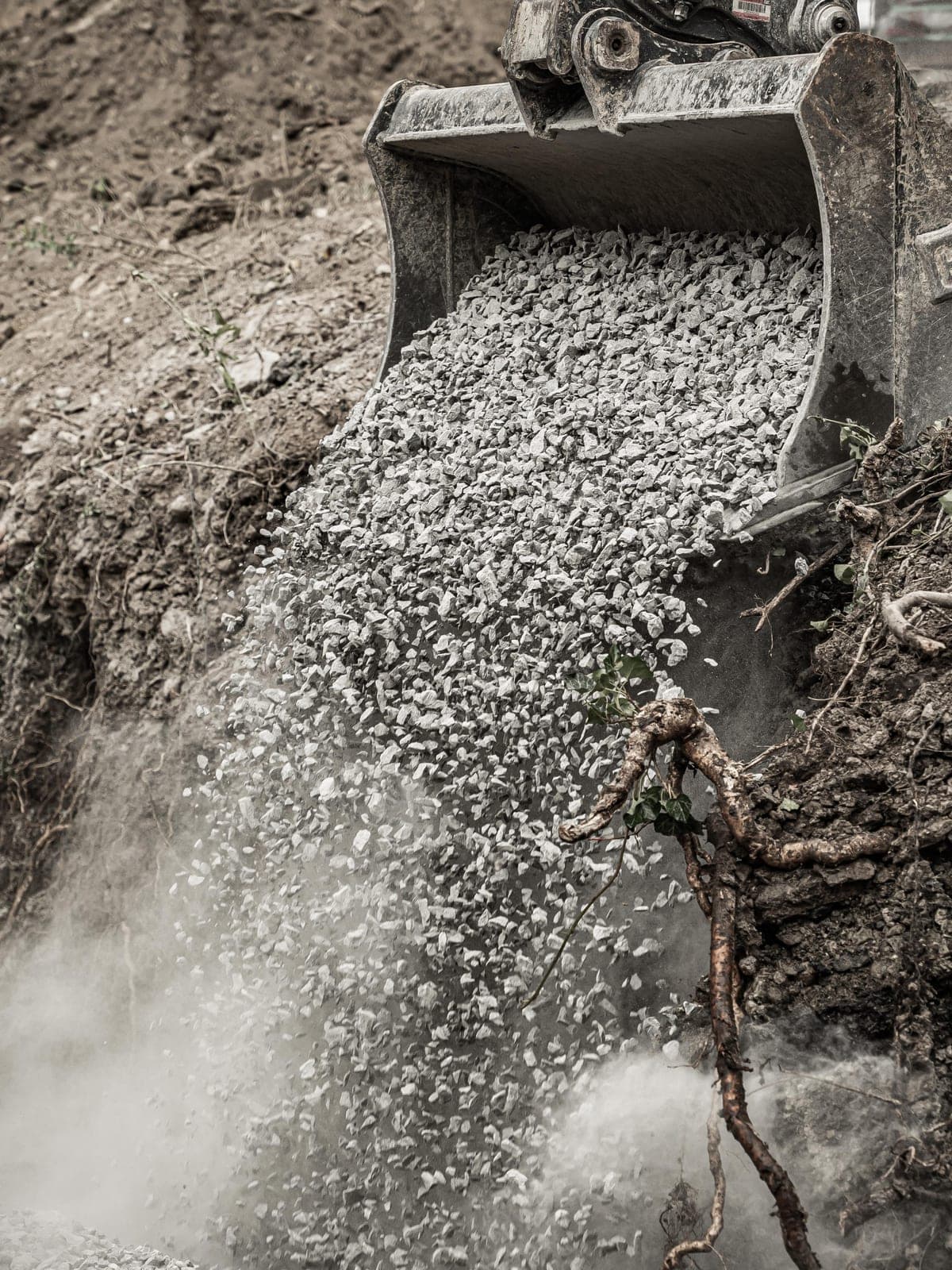 Excavator bucket pouring drainage stone into an open trench