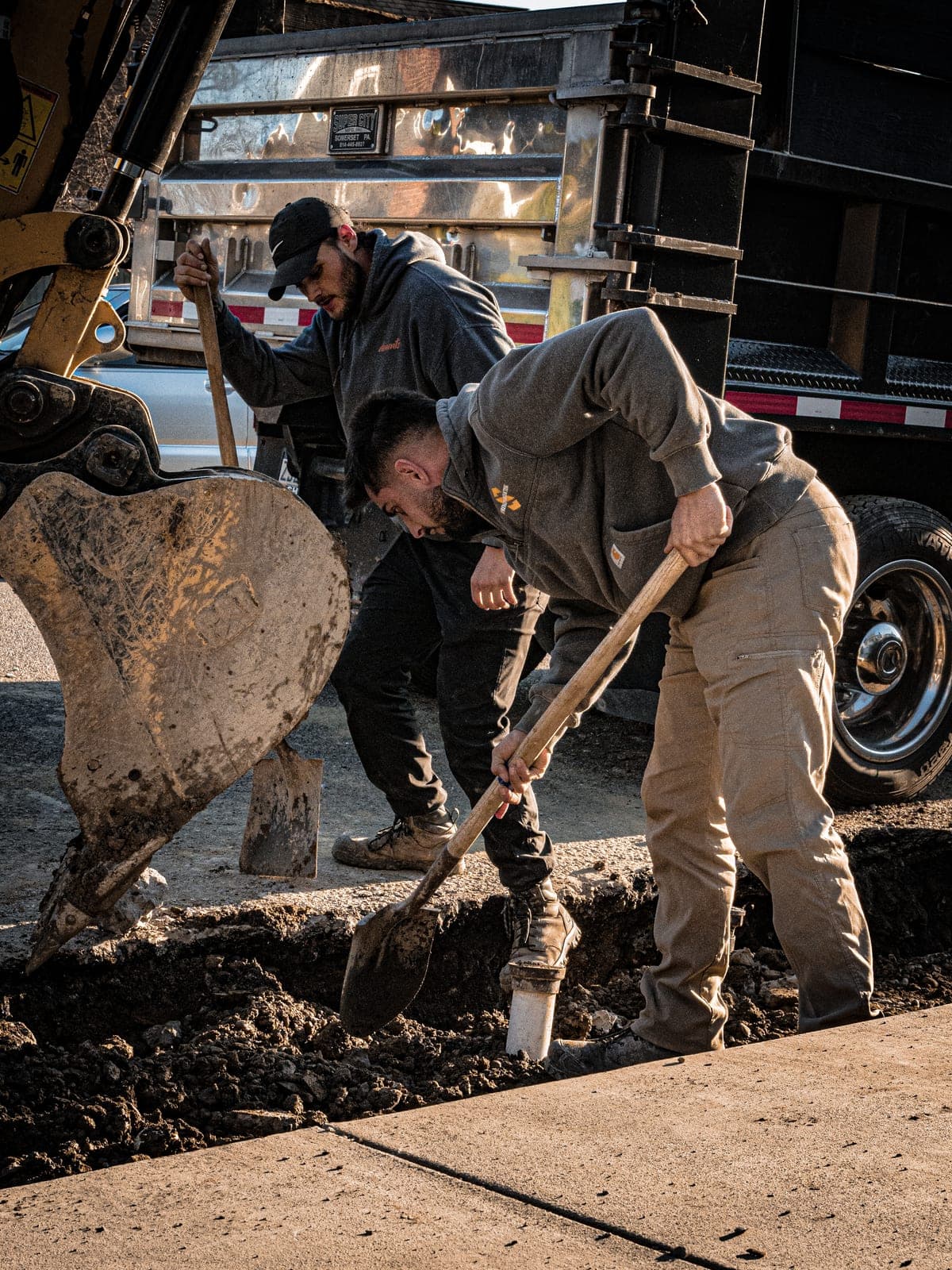 Elements crew shoveling out a grade beside the excavator at golden hour