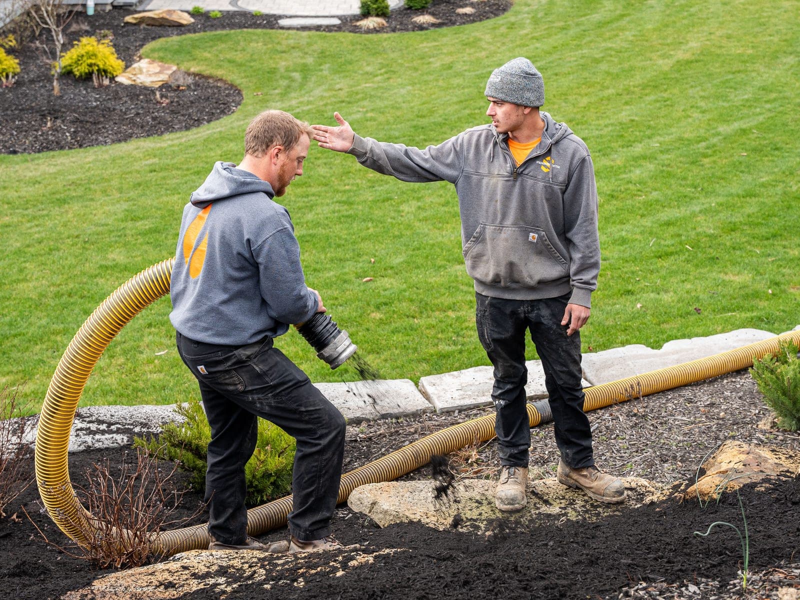 Two crew members working a mulch hose together on a finished bed