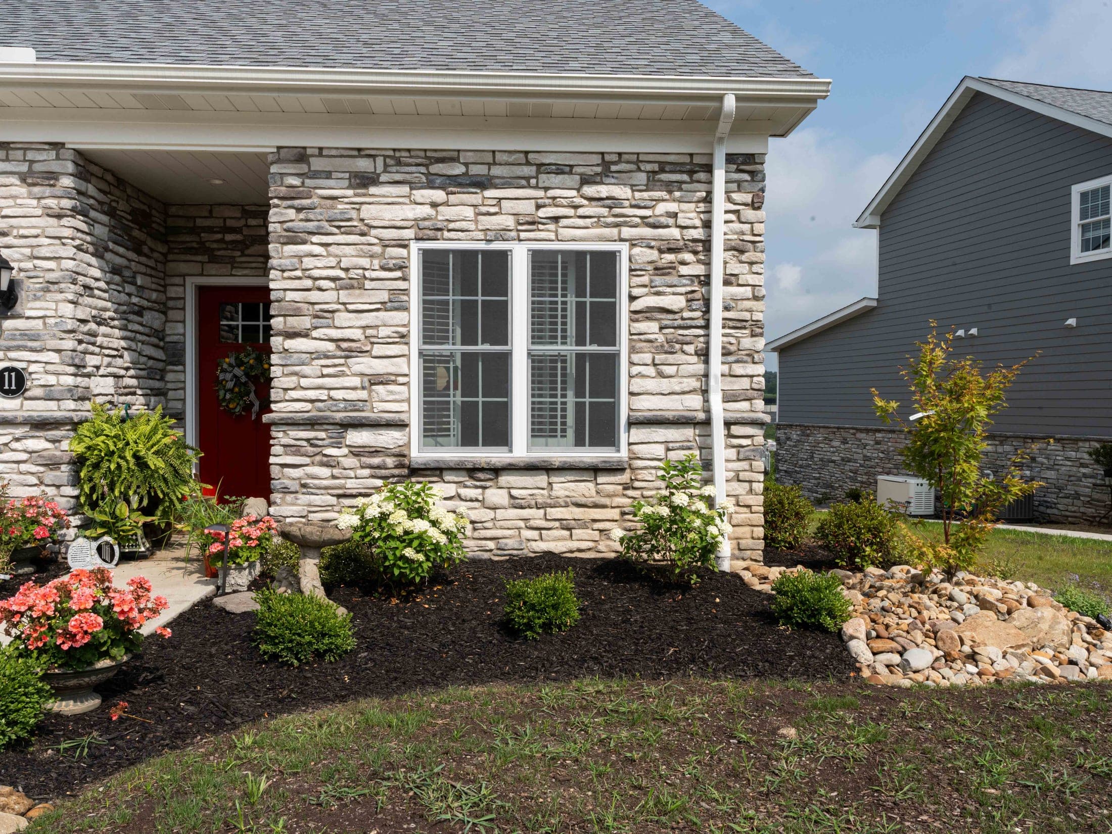 Stone facade home entrance with a red door and finished landscape beds