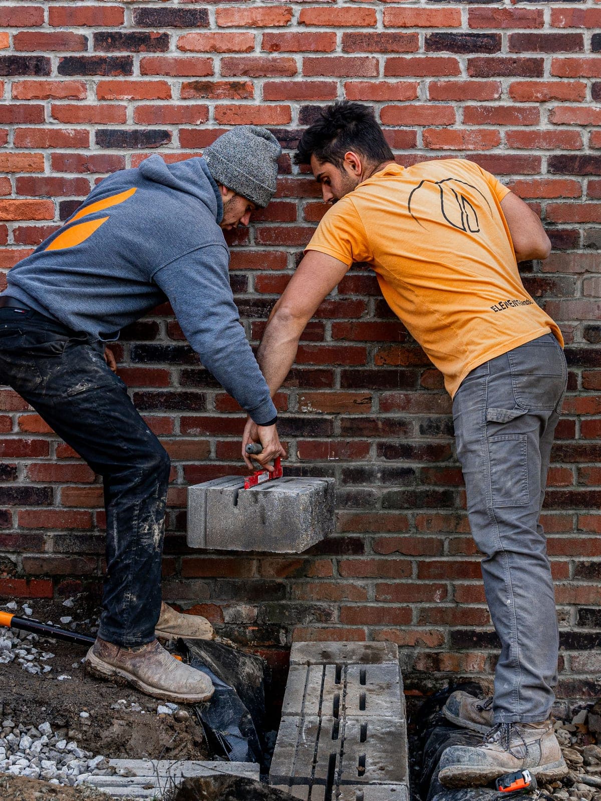 Crew setting block over drainage fabric and gravel base at the foot of a wall