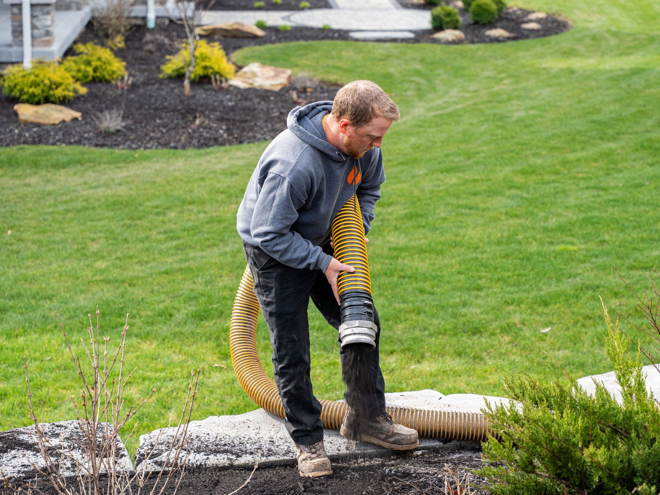 Mulch blower hose filling a landscape bed to depth