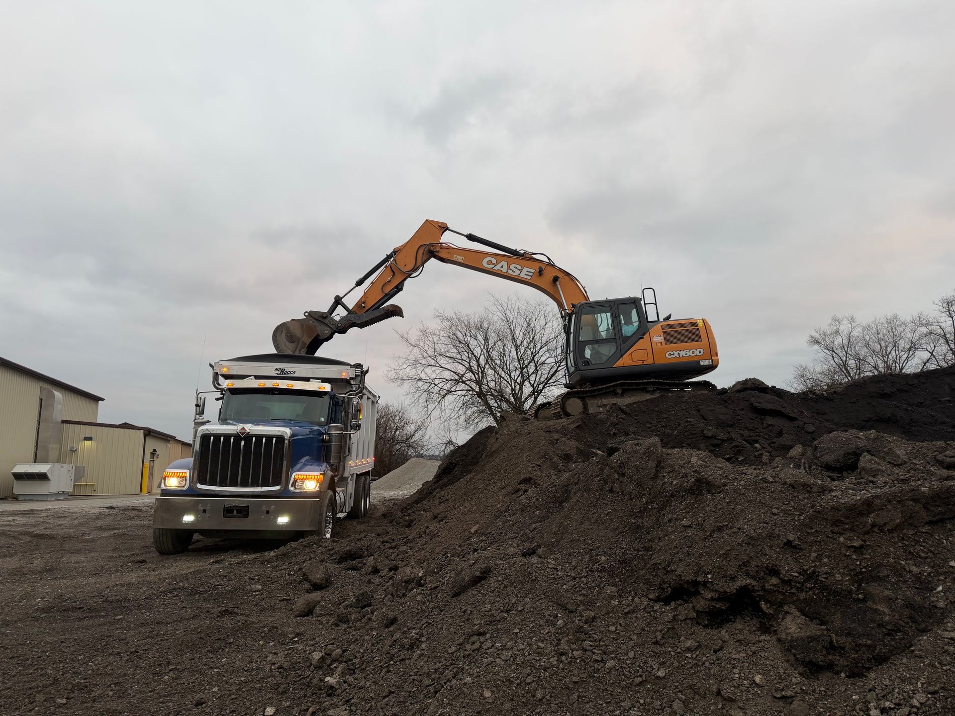 Excavator loading bulk soil into a triaxle dump truck for commercial hauling